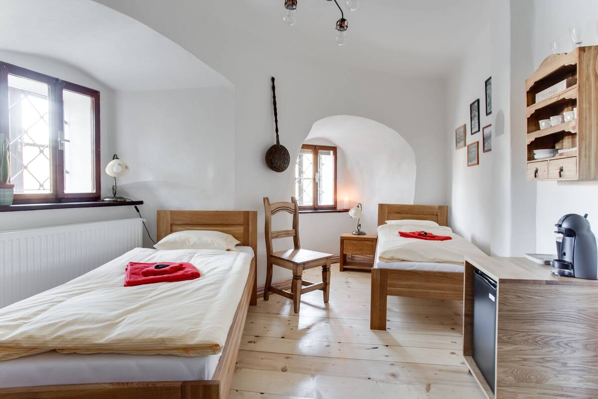 A bedroom with two wooden beds, a chair, a small table, and a built-in coffee machine.