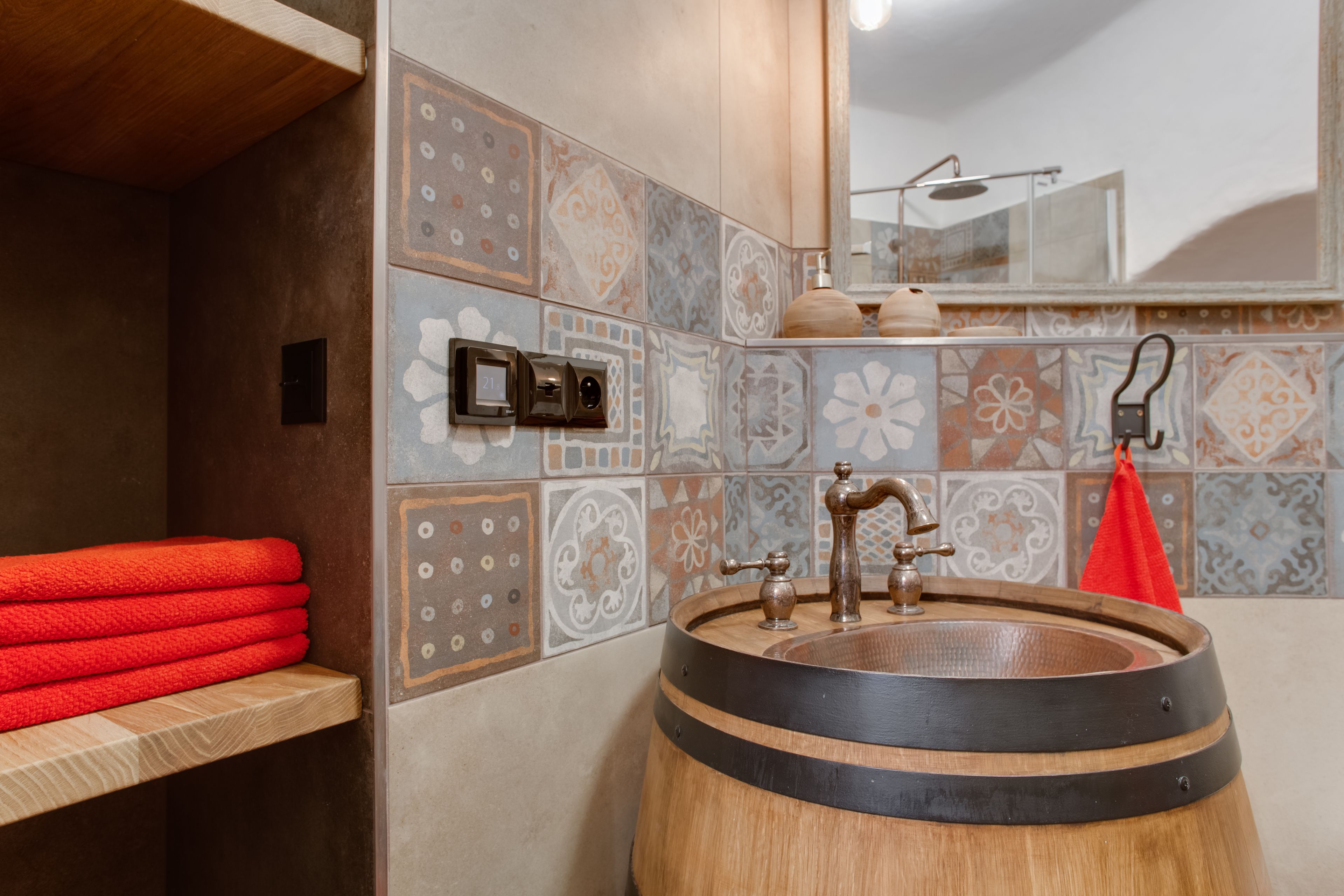 Een badkamer met een wasbak van hout, betegelde wanden en een handdoekrek met rode handdoeken.