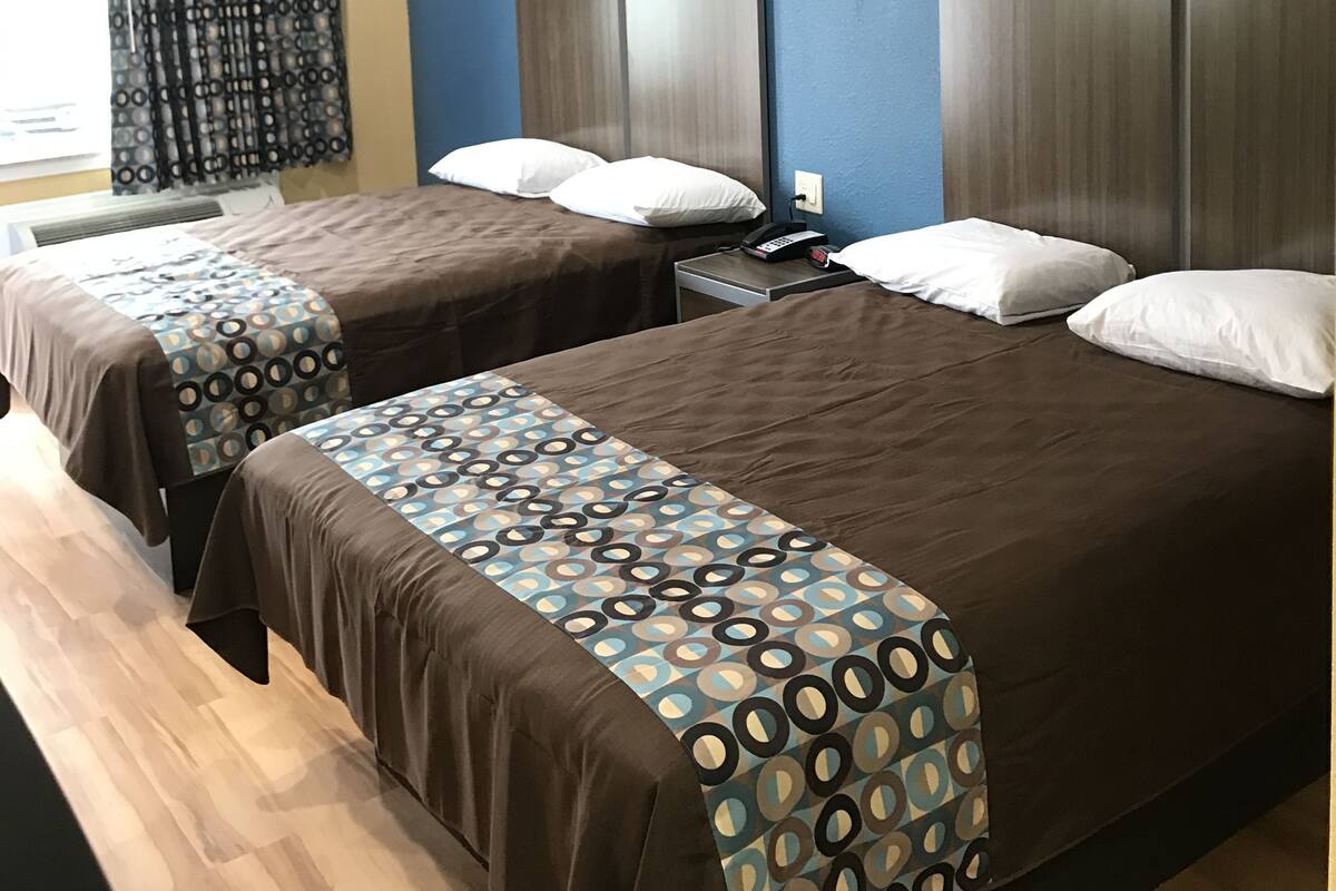 A hotel room with two beds, a nightstand, and a window with curtains.