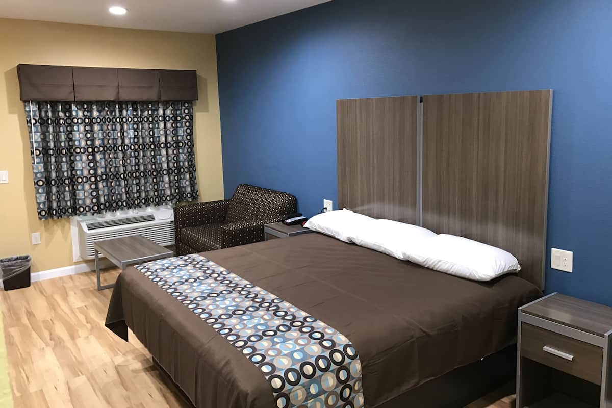 A modern hotel room with a large bed, a small seating area, and a window with curtains.