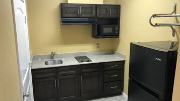 Una cocina compacta con armarios oscuros, un lavamanos de acero inoxidable, un refrigerador Haier negro y un microondas sobre la estufa.