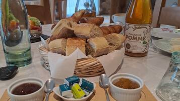 A table with a basket of assorted bread, bottles of wine, and condiments.