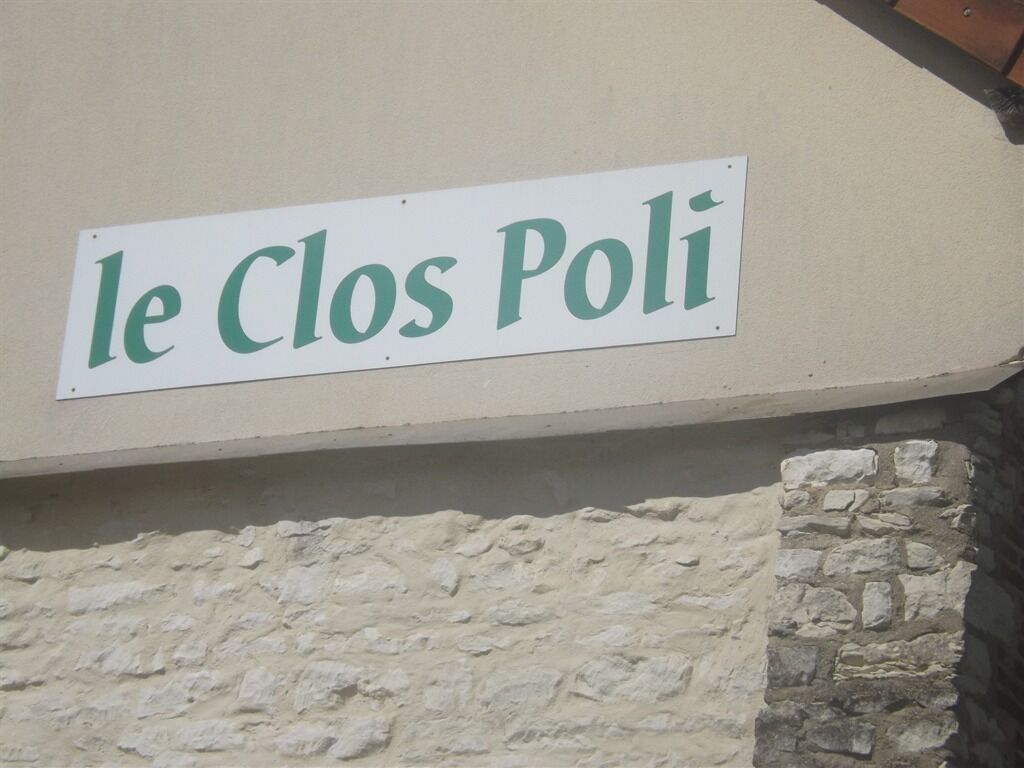 A sign with the text "le Clos Poli" on a beige wall.