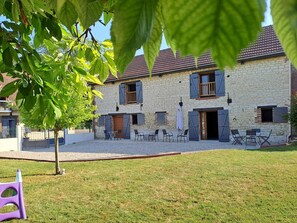A stone building with a courtyard, outdoor seating, and a tree in the foreground. - Chambres D'hôtes Le Clos Poli (Montigny-les-Monts)