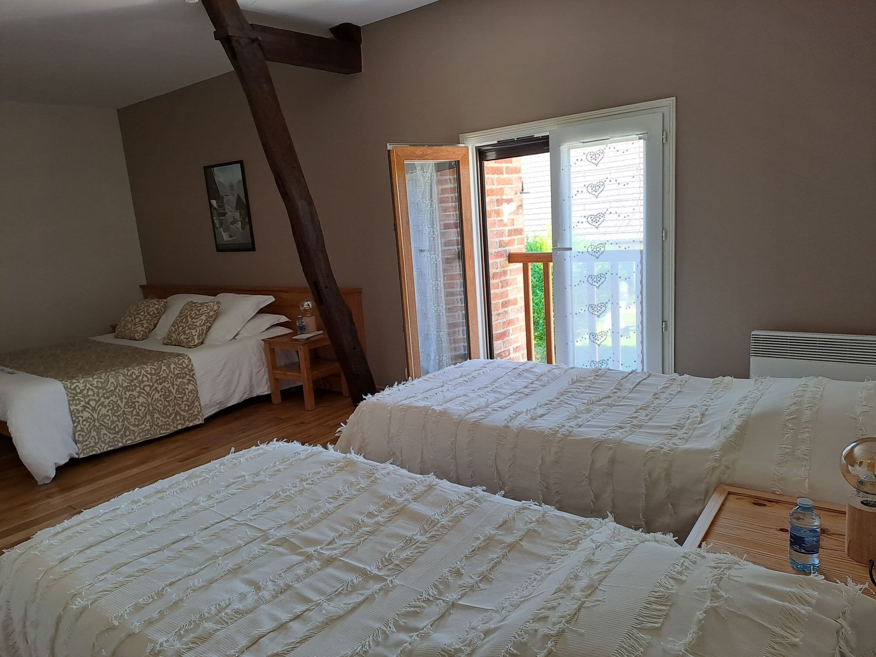 Une chambre avec deux lits, une table de chevet en bois, une chaise en bois et une fenêtre donnant sur un paysage verdoyant.