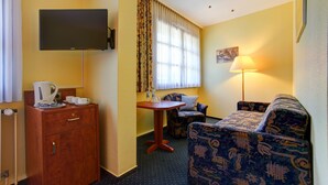 A hotel room with a bed, a sofa, a small table, a TV mounted on the wall, and a window with curtains. - Hotel Garni Fock Und Oben (Hamburg)