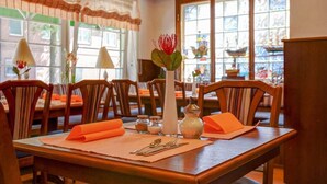 A dining area with wooden tables, orange napkins, and a vase with a red flower centerpiece. - Hotel Garni Fock Und Oben (Hamburg)