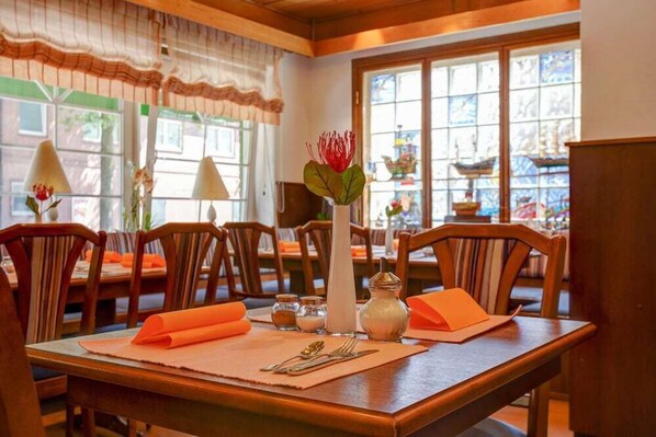 Comedor con mesas de madera, servilletas naranjas y un centro de mesa con una flor roja en un jarrón.