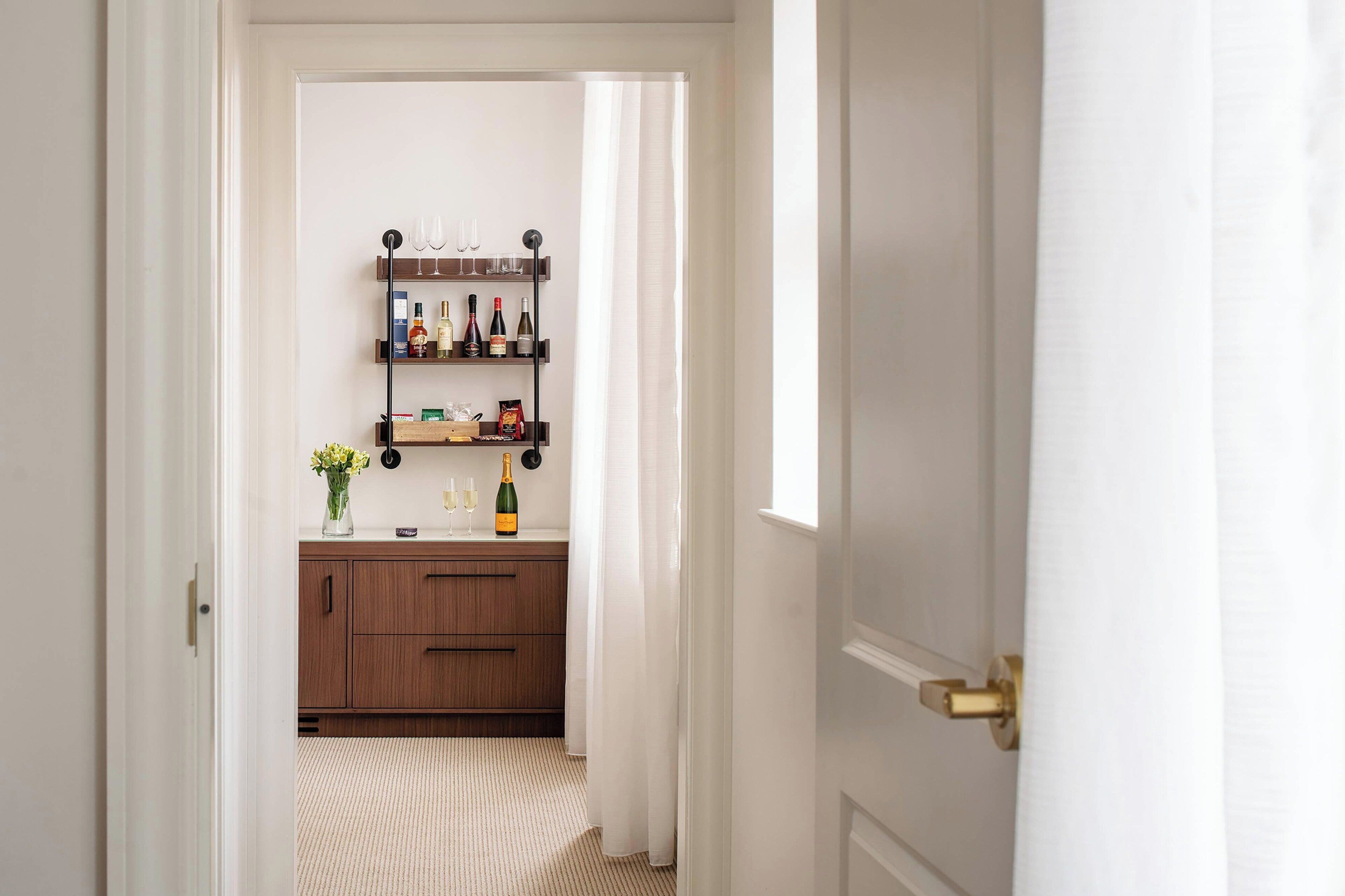A hallway leading to a kitchen with wooden cabinets, a wine rack, and a vase of flowers.