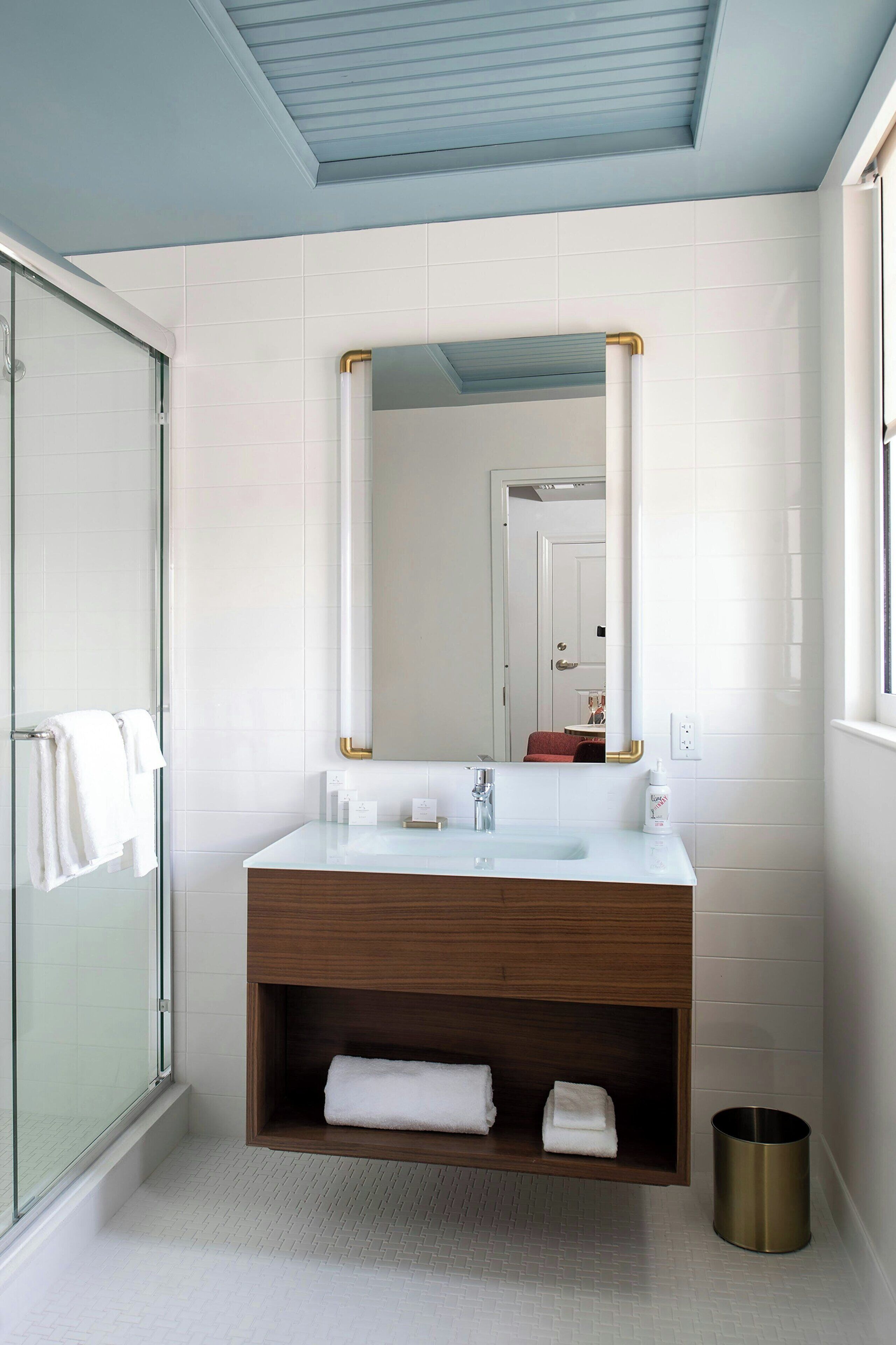 A modern bathroom with a glass shower enclosure, a white sink with a wooden vanity, and a large mirror with gold frame.