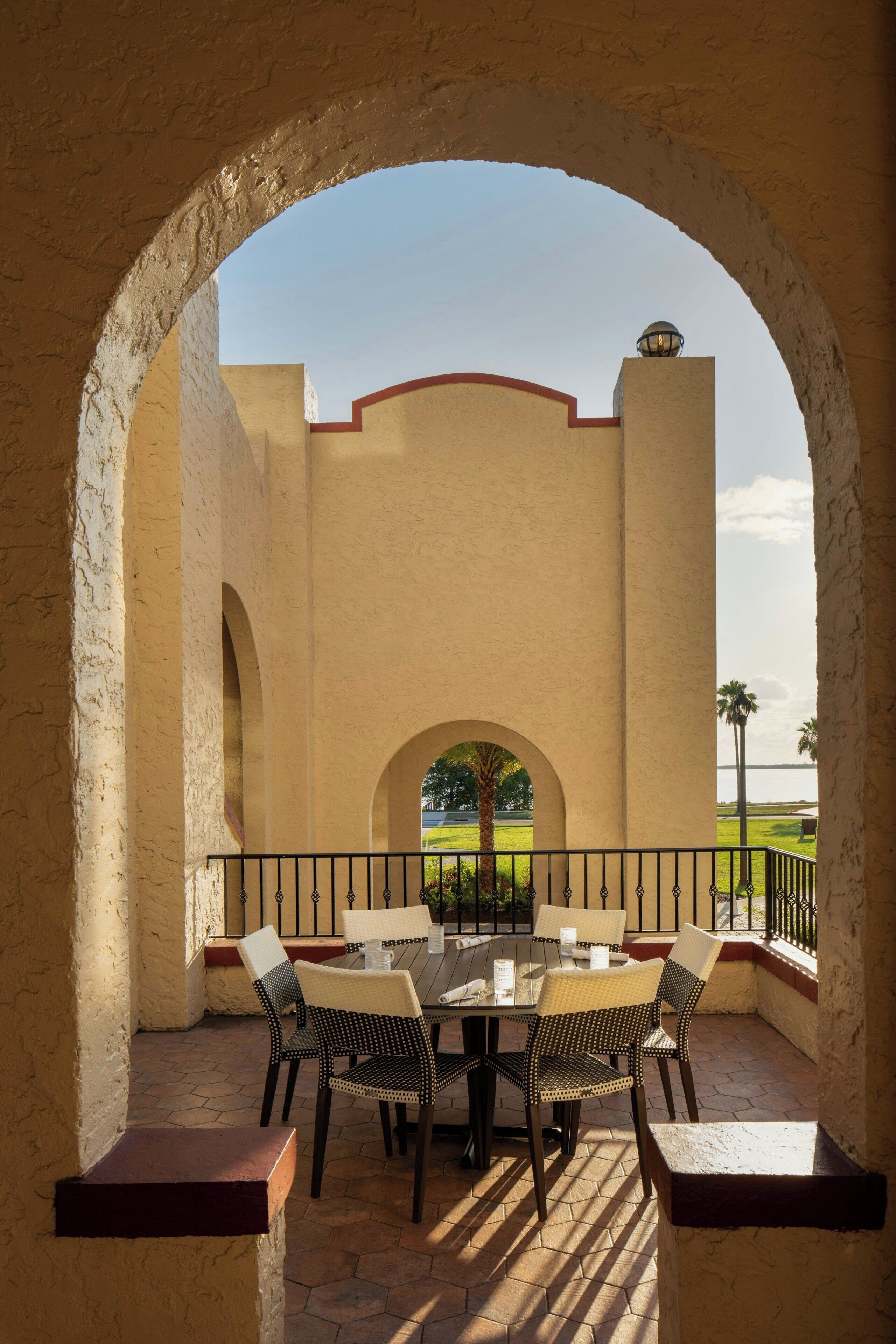 Eine Terrasse im Freien mit Tisch und Stühlen, einem Bogen und Blick auf eine entfernte Landschaft.