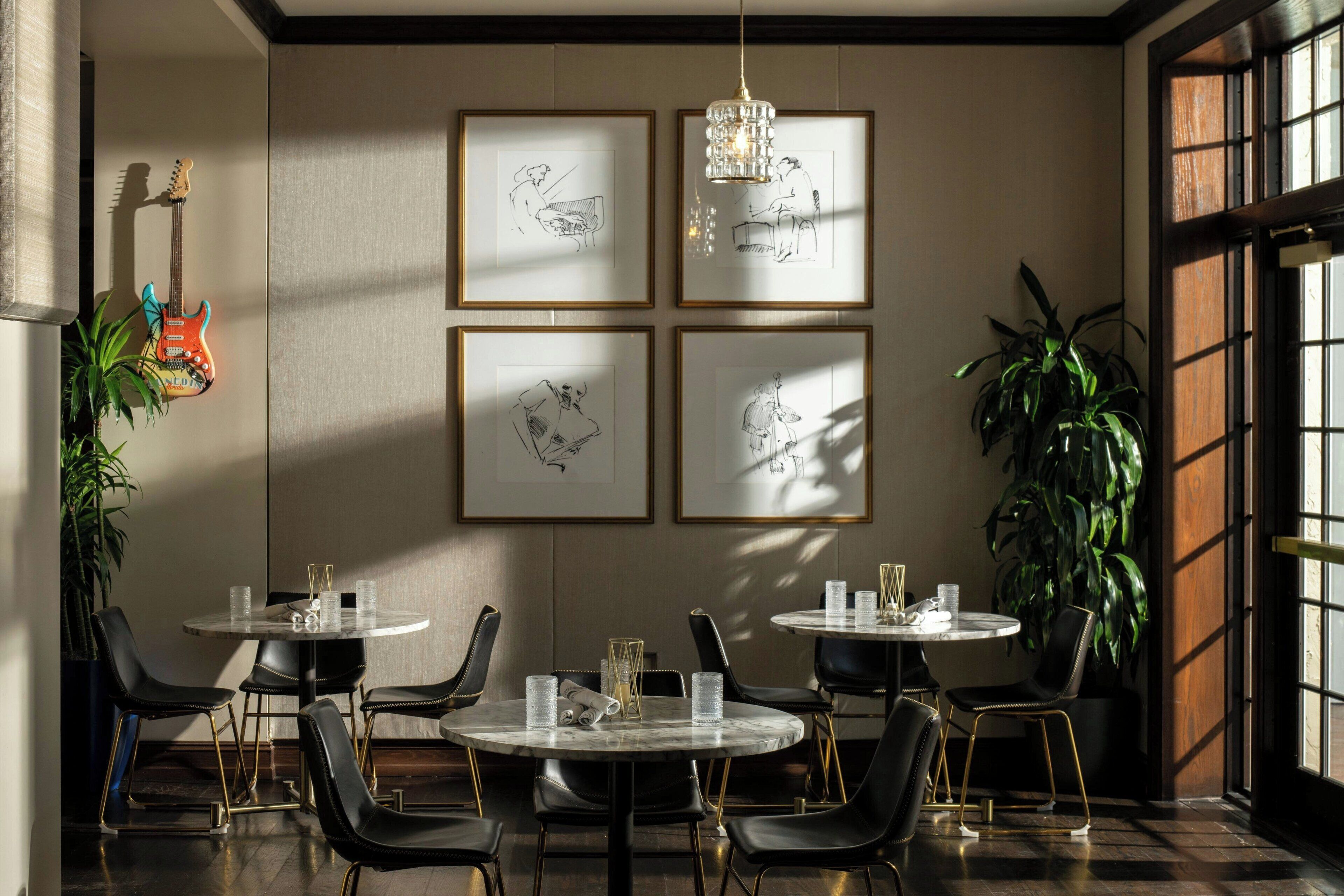 A dining area with round tables, black chairs, and framed sketches on the wall.