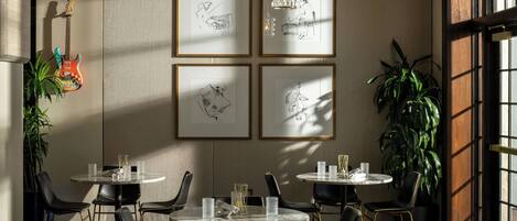 A dining area with round tables, black chairs, and framed sketches on the wall.
