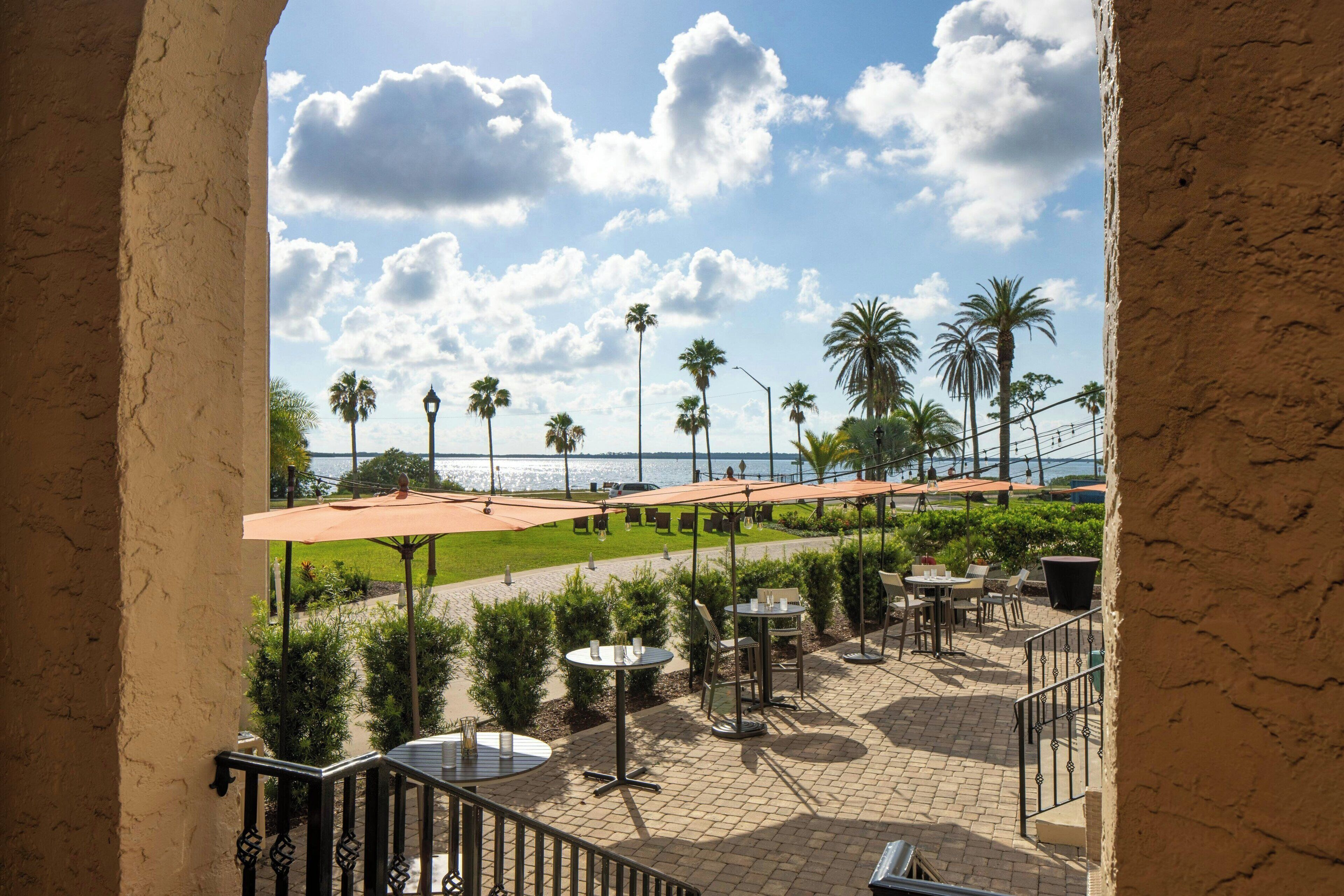 A terrace with outdoor seating, palm trees, and a view of the sea.