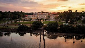 A large hotel with a central courtyard, palm trees, and a body of water reflecting the sky.