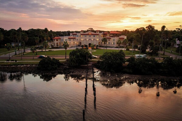Un hotel grande con un patio central, palmeras y una masa de agua que refleja el cielo.