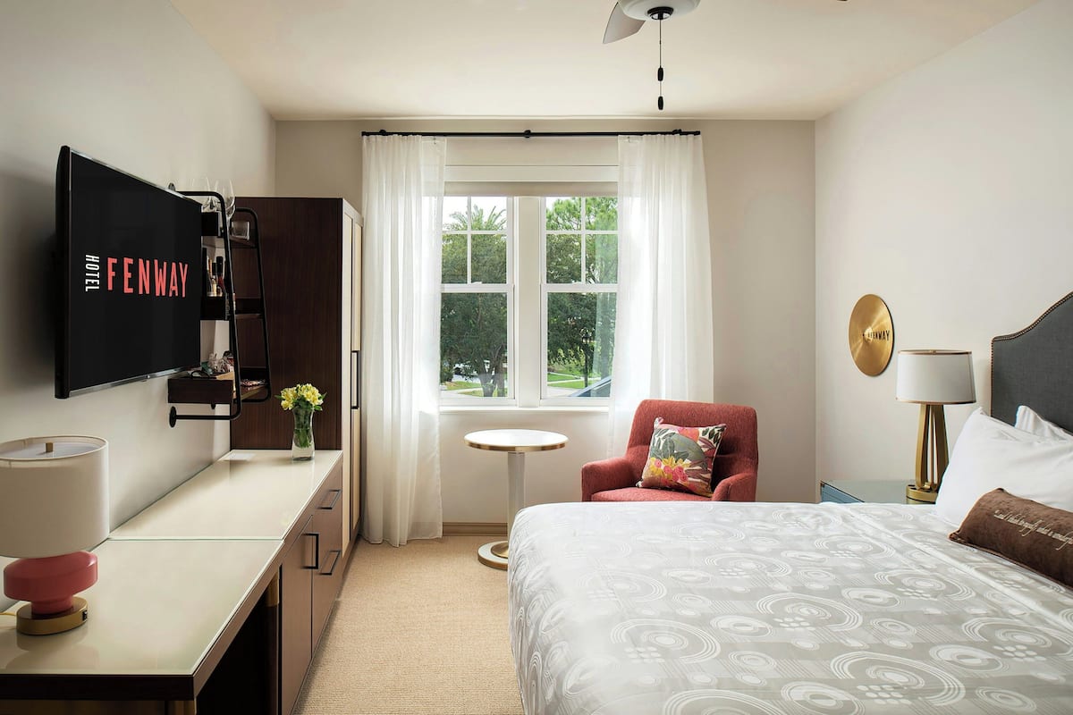 A hotel room with a bed, a desk, a TV, a chair, a small table, and a window with curtains.
