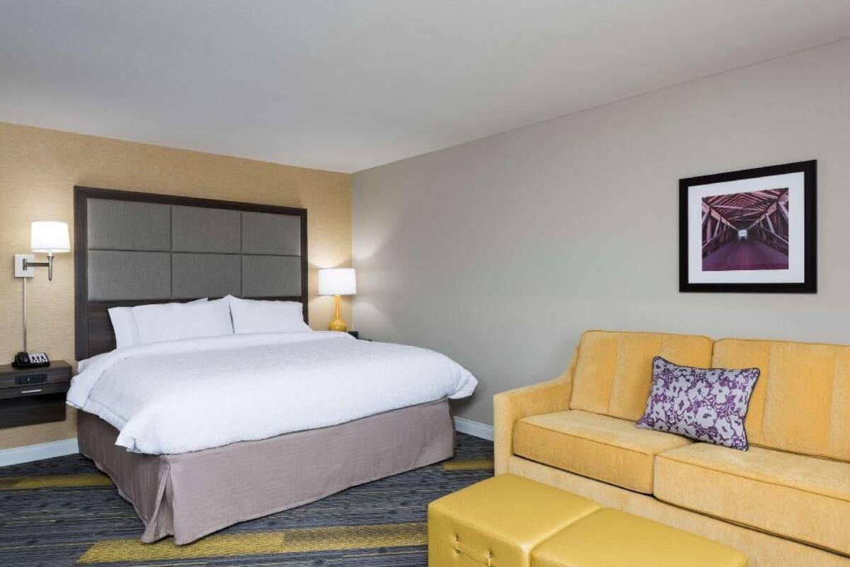A hotel room with a bed, bedside lamps, a sofa, a chair, a small table, and a framed picture on the wall.