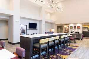 Un moderno vestíbulo de hotel con una barra alargada, diversas opciones de asientos, un televisor de pantalla plana y una estación de café.