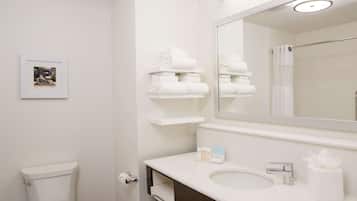 Un baño con inodoro, lavabo, espejo y repisas con toallas dobladas.