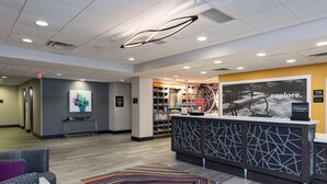 A hotel reception area with a modern design, including a reception desk, seating area, and a wall with a 'explore' sign. - Hampton Inn & Suites West Lafayette (West Lafayette)