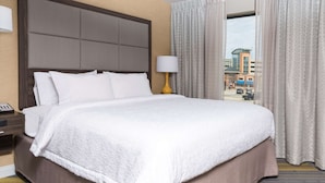 A hotel room with a large bed, a nightstand, a lamp, and a view of the outside. - Hampton Inn & Suites West Lafayette (West Lafayette)