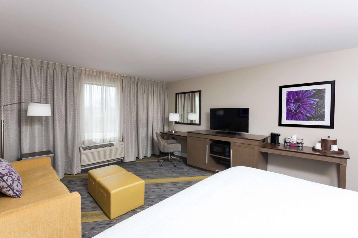 A hotel room with a bed, a desk, a chair, a television, and a large window with curtains.
