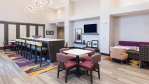 A modern hotel lobby with a bar area, seating arrangements, and a television. - Hampton Inn & Suites West Lafayette (West Lafayette)