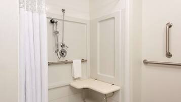 Un baño con ducha, barras de apoyo, un asiento y un perchero para toallas.