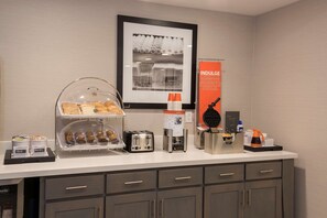 A breakfast bar with a coffee machine, toaster, and waffle maker. There are also condiments and a framed picture on the wall. - Hampton Inn & Suites West Lafayette (West Lafayette)