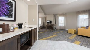 A hotel room with a kitchenette, a living area with a sofa and a TV, and a large window with curtains. - Hampton Inn & Suites West Lafayette (West Lafayette)