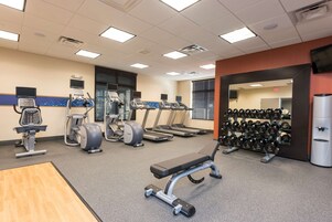 A gym with treadmills, elliptical machines, a bench press, and a rack of dumbbells.