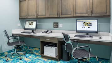 A workspace with two desks, each with a computer, keyboard, and mouse. There are two office chairs, a printer, and a cabinet above the desks.