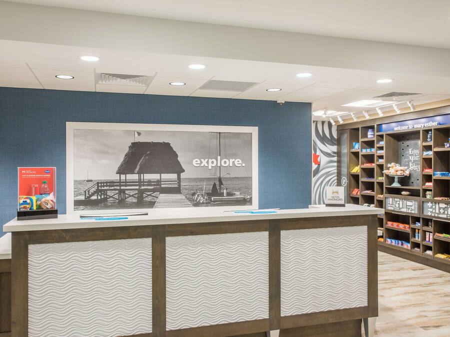 A reception desk with a large poster of a pier and boats, a wooden counter, and shelves with various items.