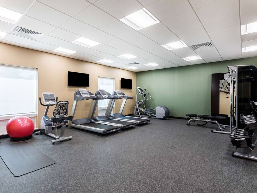 Academia com esteiras, bicicletas ergométricas, uma bola de exercícios vermelha e aparelhos de musculação.