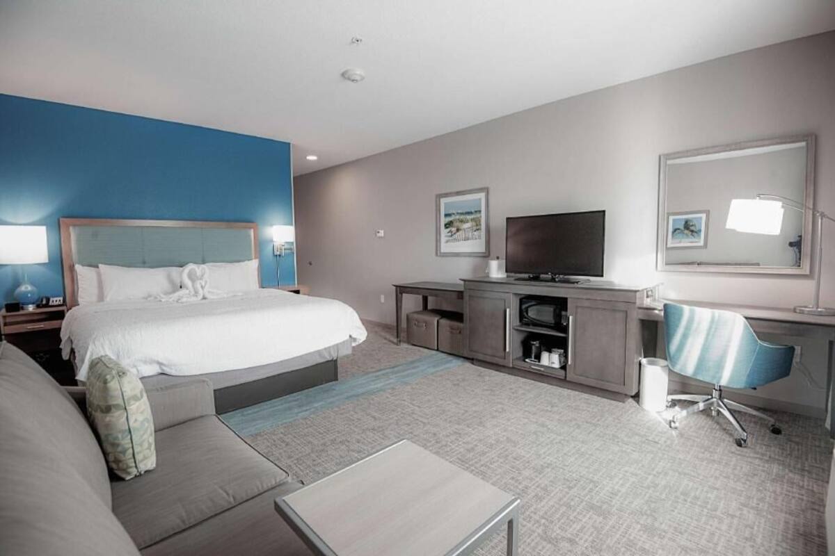 Una habitación de hotel con cama, escritorio, televisor, silla y sofá.