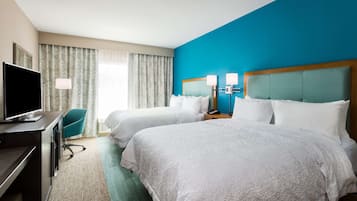 A hotel room with two beds, a desk with a TV, and a desk lamp.