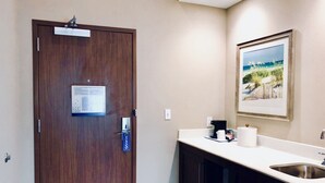 Une chambre d’hôtel avec une porte en bois, un tableau d’affichage sur lequel est affiché un plan d’évacuation, un lavabo et un tableau encadré accroché au mur.