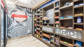 Un magasin dont les étagères sont remplies de collations et de friandises, avec une enseigne indiquant « Friandises » et une autre qui dit « Bienvenue à Mary Esther ».