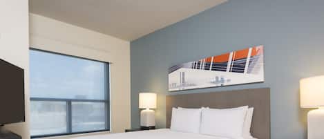 Een hotelkamer met een groot bed, twee nachtkastjes met lampen, een flatscreen-tv en een raam met uitzicht op de stad.