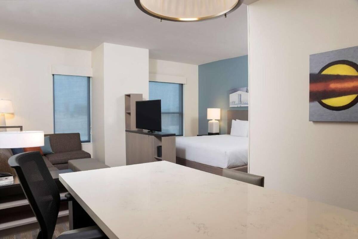 A hotel room with a bed, a desk, a television, and a painting on the wall.