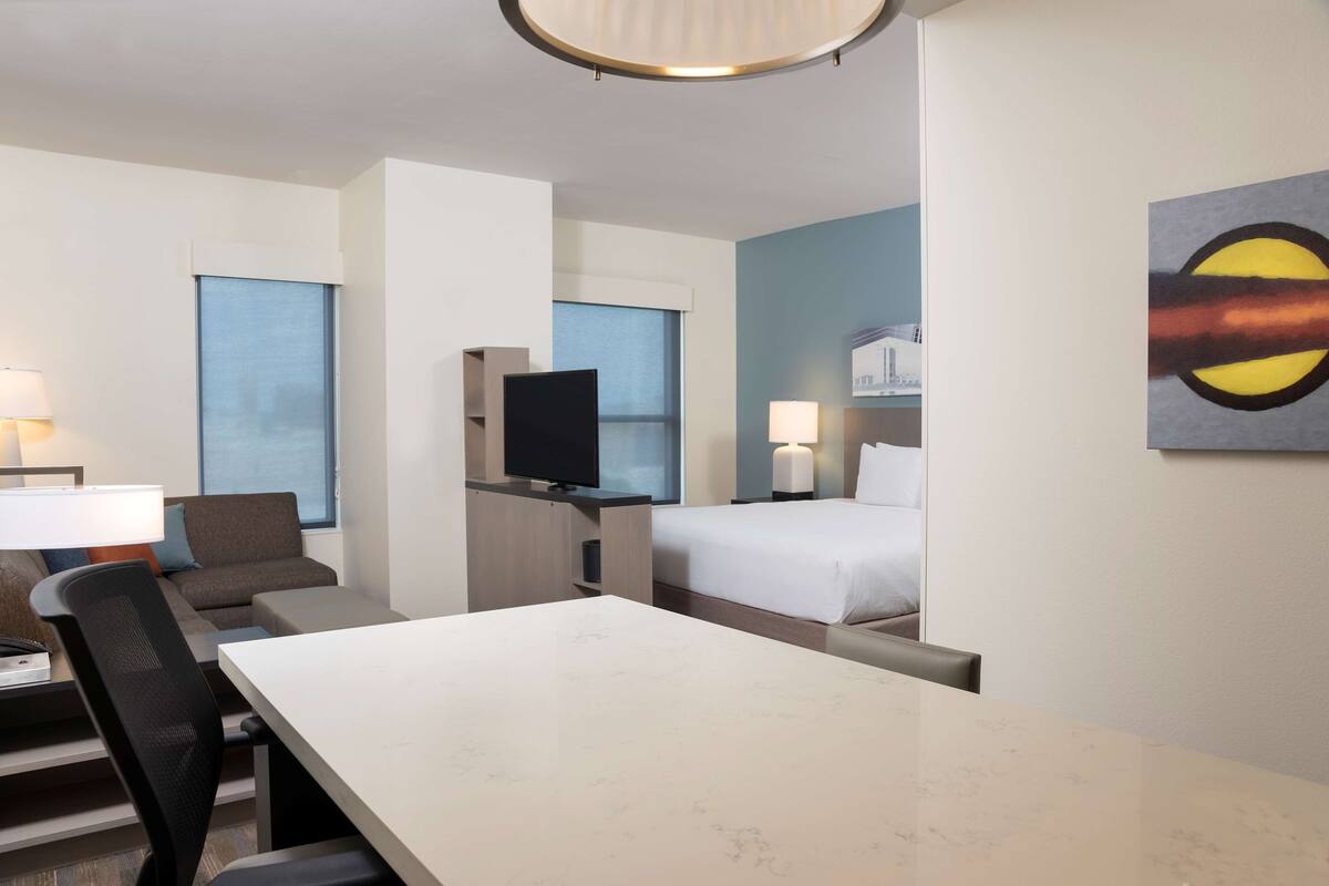 Una habitación de hotel con cama, escritorio, silla, televisor y un cuadro en la pared.