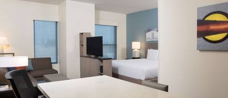 A hotel room with a bed, a desk, a chair, a television, and a painting on the wall.