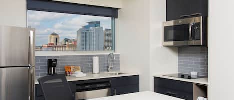 A modern kitchen with a stainless steel refrigerator, a built-in dishwasher, a microwave, and a window with a city view.