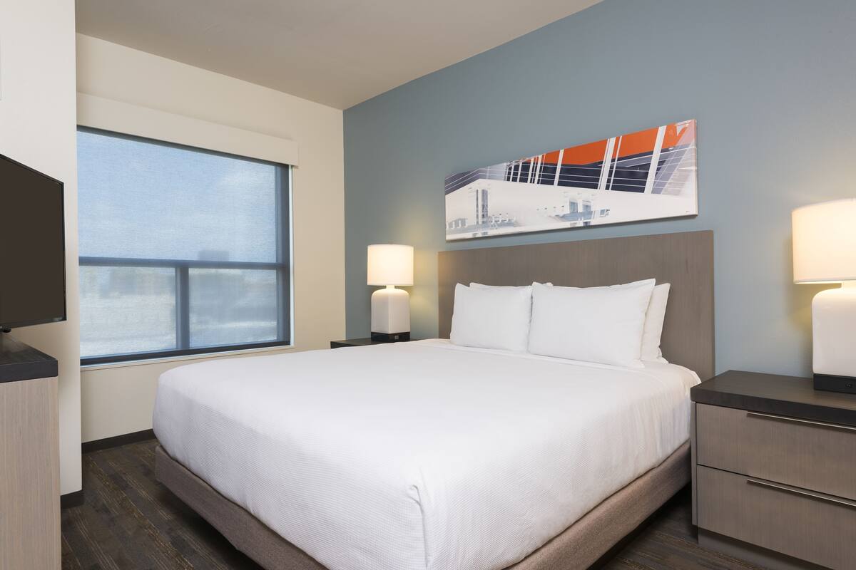 A hotel room with a large bed, bedside tables, a TV, and a window.