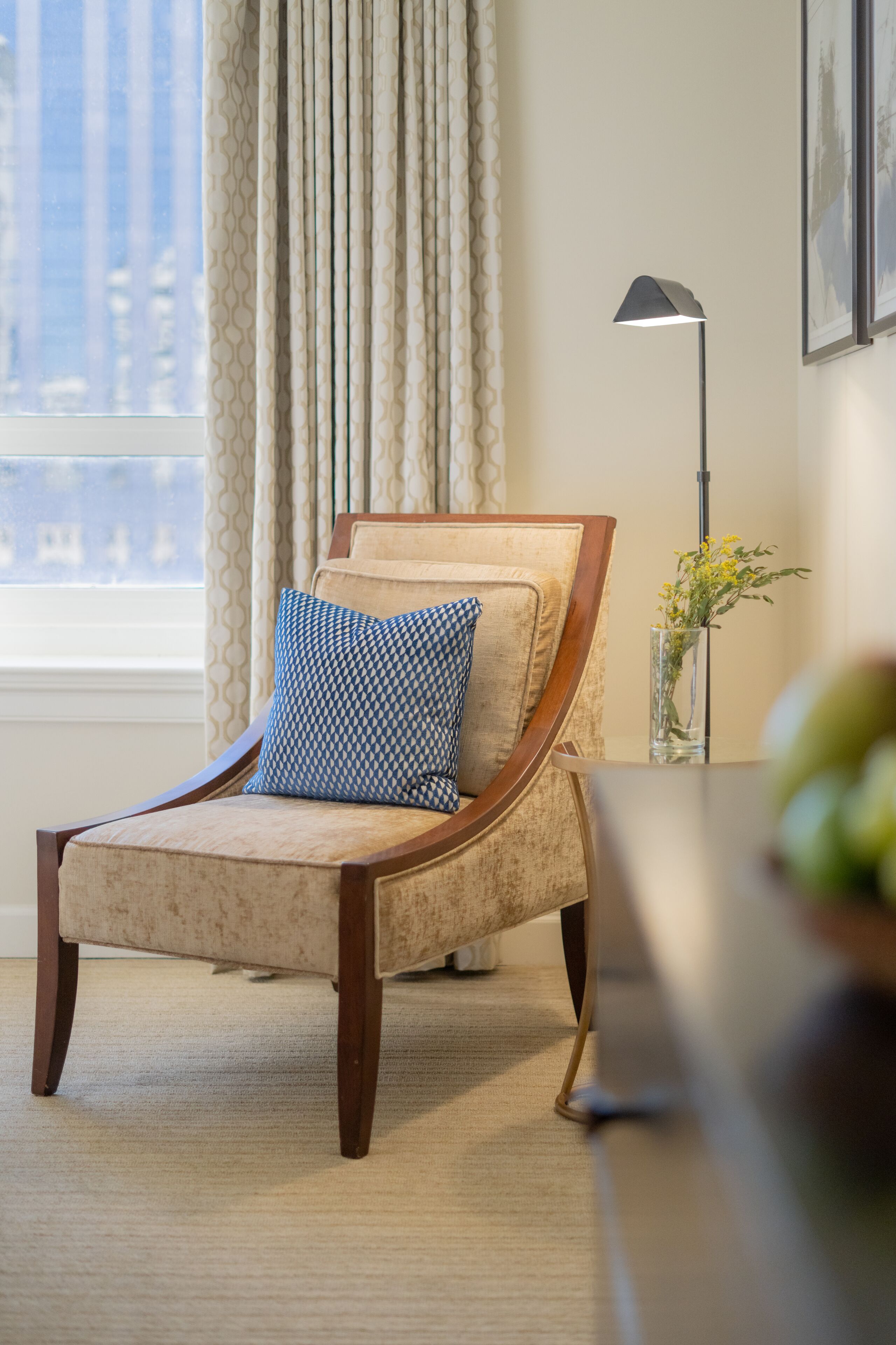 A lounge chair with a patterned cushion, a vase with flowers, and a floor lamp.