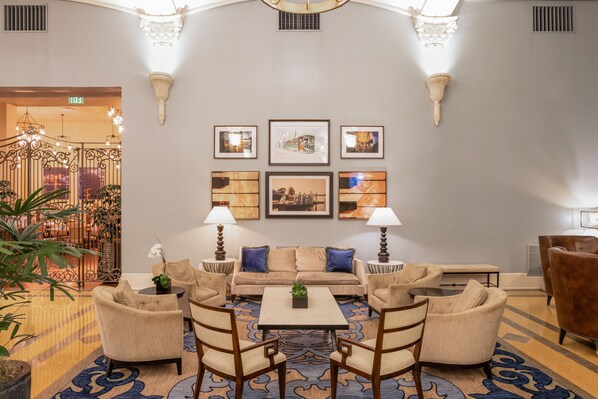 A lobby with a sofa, armchairs, a coffee table, and lamps. There are framed pictures on the wall and a patterned carpet.