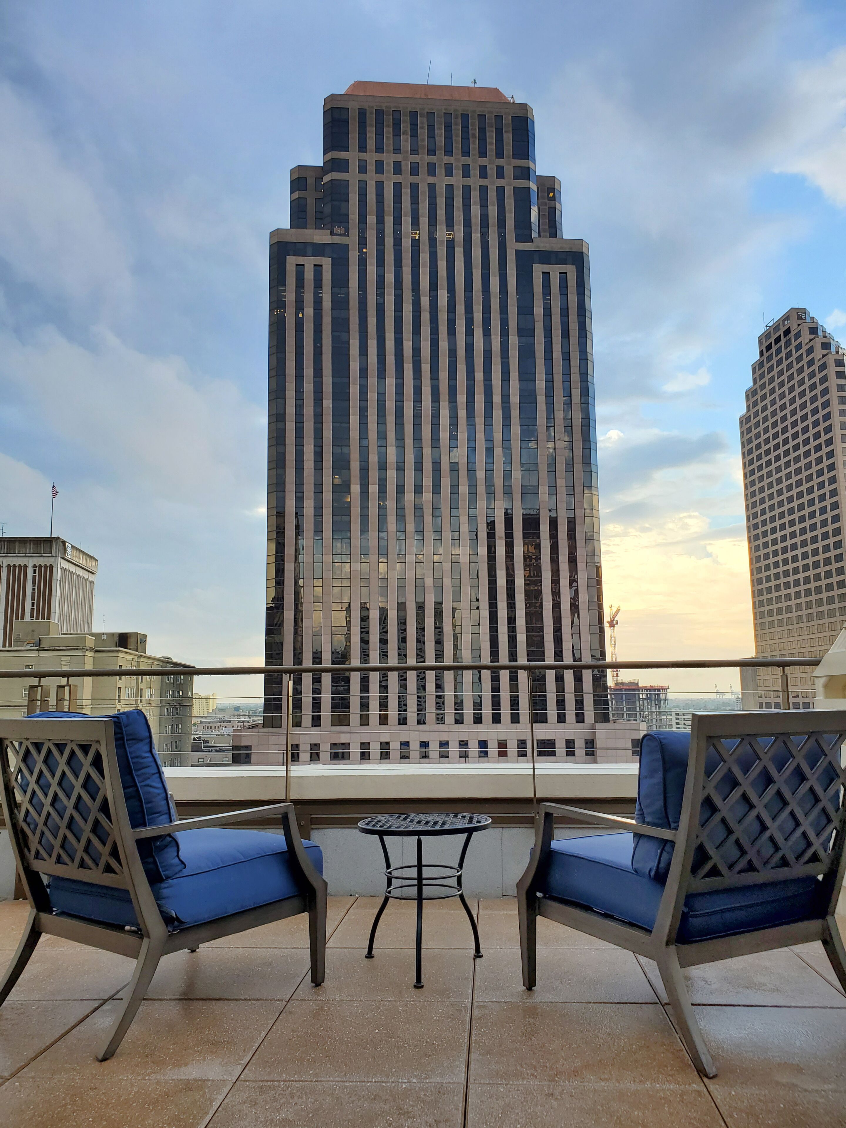 A terrace with two blue cushioned chairs and a small table, overlooking a cityscape with tall buildings.