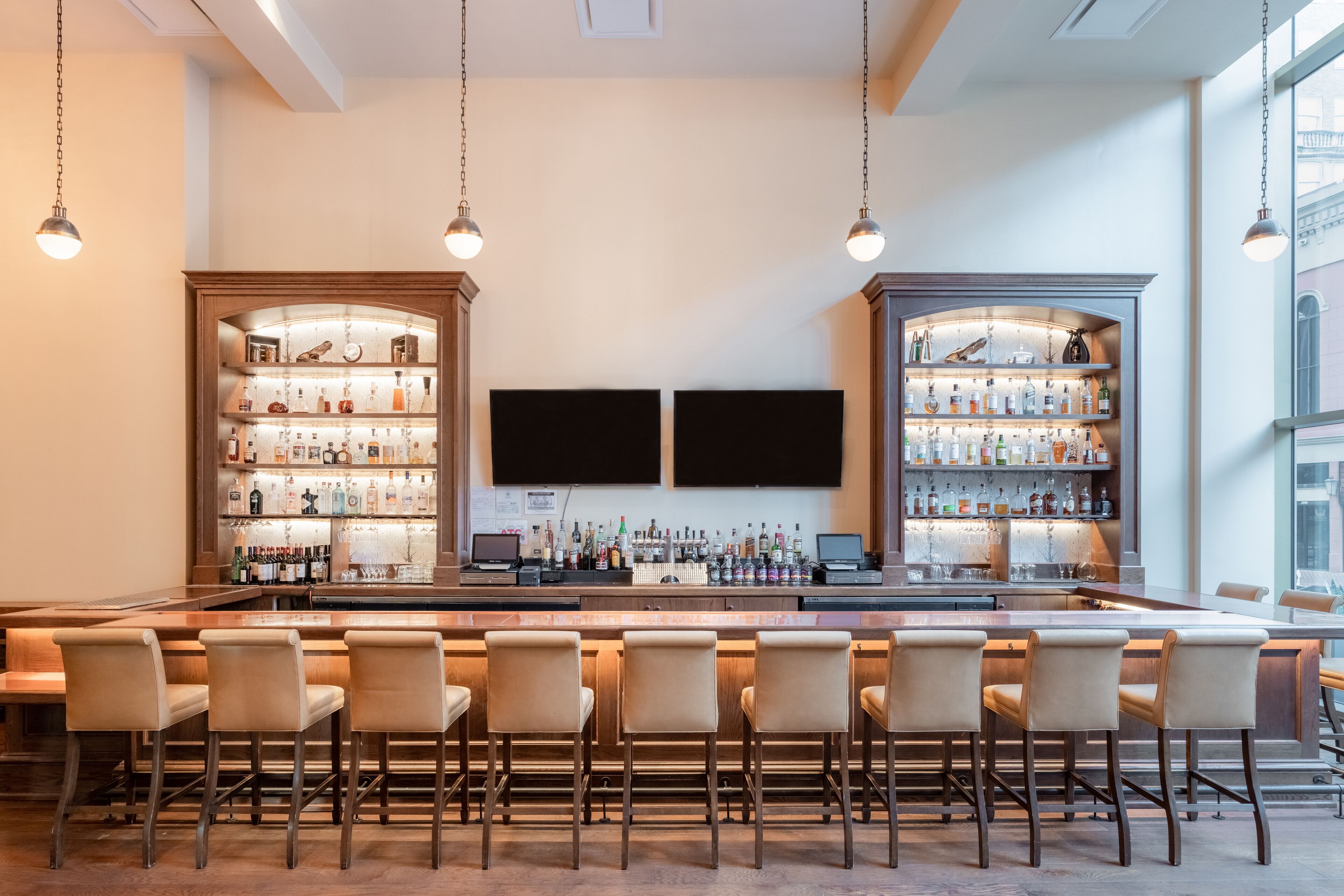 A bar area with a long counter, multiple bar stools, and shelves stocked with bottles.