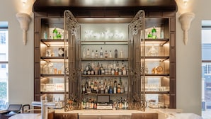 A bar area with a marble countertop, leather bar stools, and a variety of bottles and glasses on shelves.